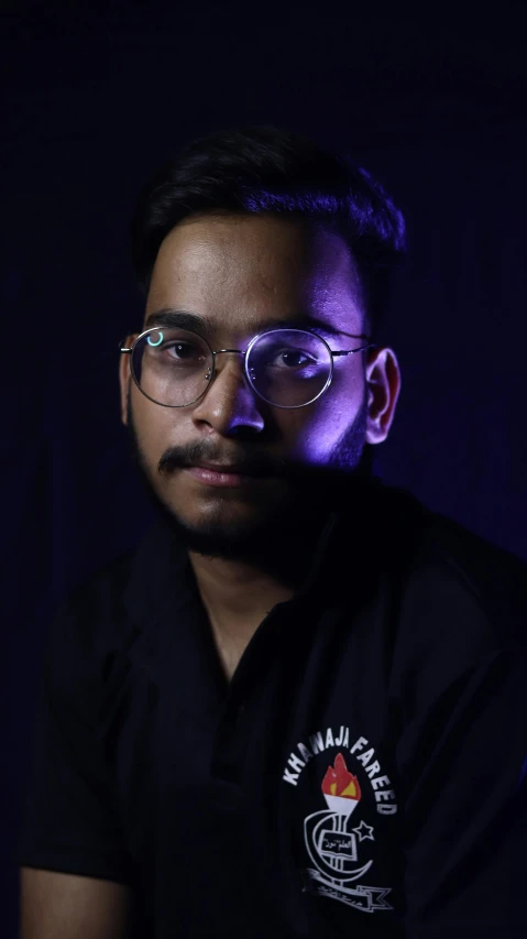 a man wearing glasses and a black shirt, a character portrait, inspired by Saurabh Jethani, pexels contest winner, hurufiyya, purple ambient light, discord profile picture, taken with sony alpha 9, androgynous person