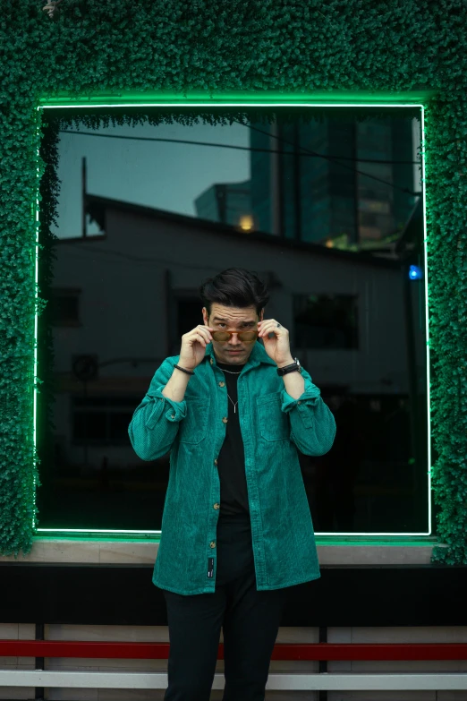 a man standing in front of a mirror talking on a cell phone, an album cover, by Alejandro Obregón, pexels contest winner, green neon signs, asian man, man with glasses, standing outside a house