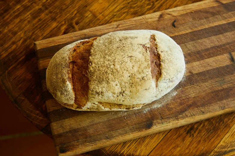 a loaf of bread sitting on top of a wooden cutting board, sandstone, thumbnail, round head, very large