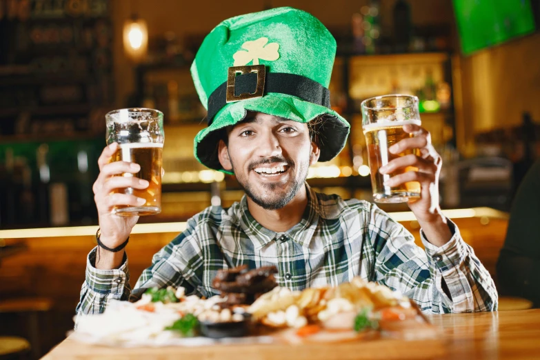 a man sitting at a table with two glasses of beer, pots of gold, 👰 🏇 ❌ 🍃, wearing a hat, offering a plate of food