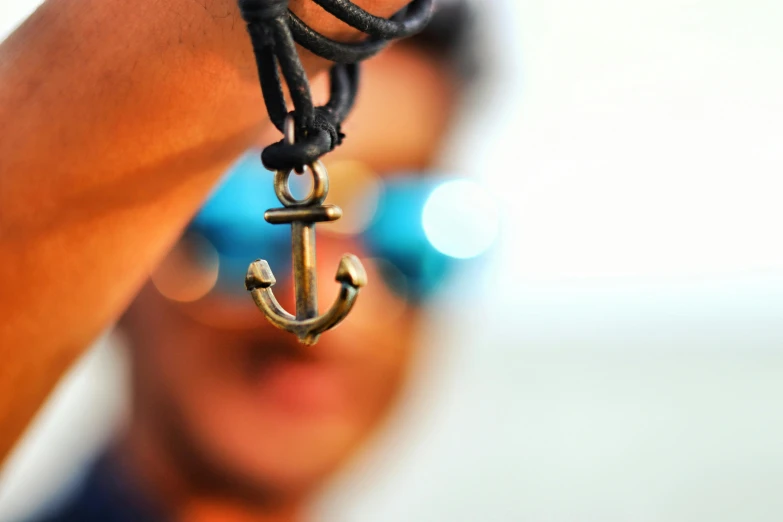 a close up of a person holding a necklace with an anchor on it, by Niko Henrichon, trending on pexels, avatar image, shades, attractive and good looking, blurred background