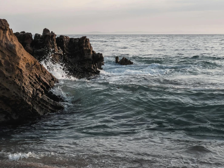 a man riding a surfboard on top of a wave covered beach, inspired by Elsa Bleda, unsplash, romanticism, sharp spiky rocks, with lots of dark grey rocks, malibu canyon, photo taken from a boat