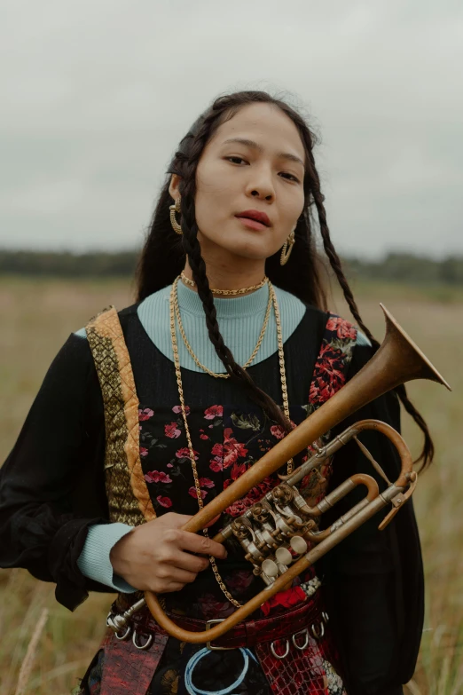 a woman standing in a field holding a trumpet, bao pham, brass, indigenous, asian descent