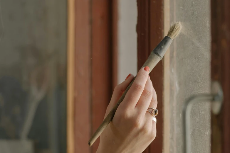 a woman holding a brush in front of a window, inspired by Balthus, featured on unsplash, arts and crafts movement, fine texture detail, rustic and weathered, payne's grey and venetian red, environmental shot