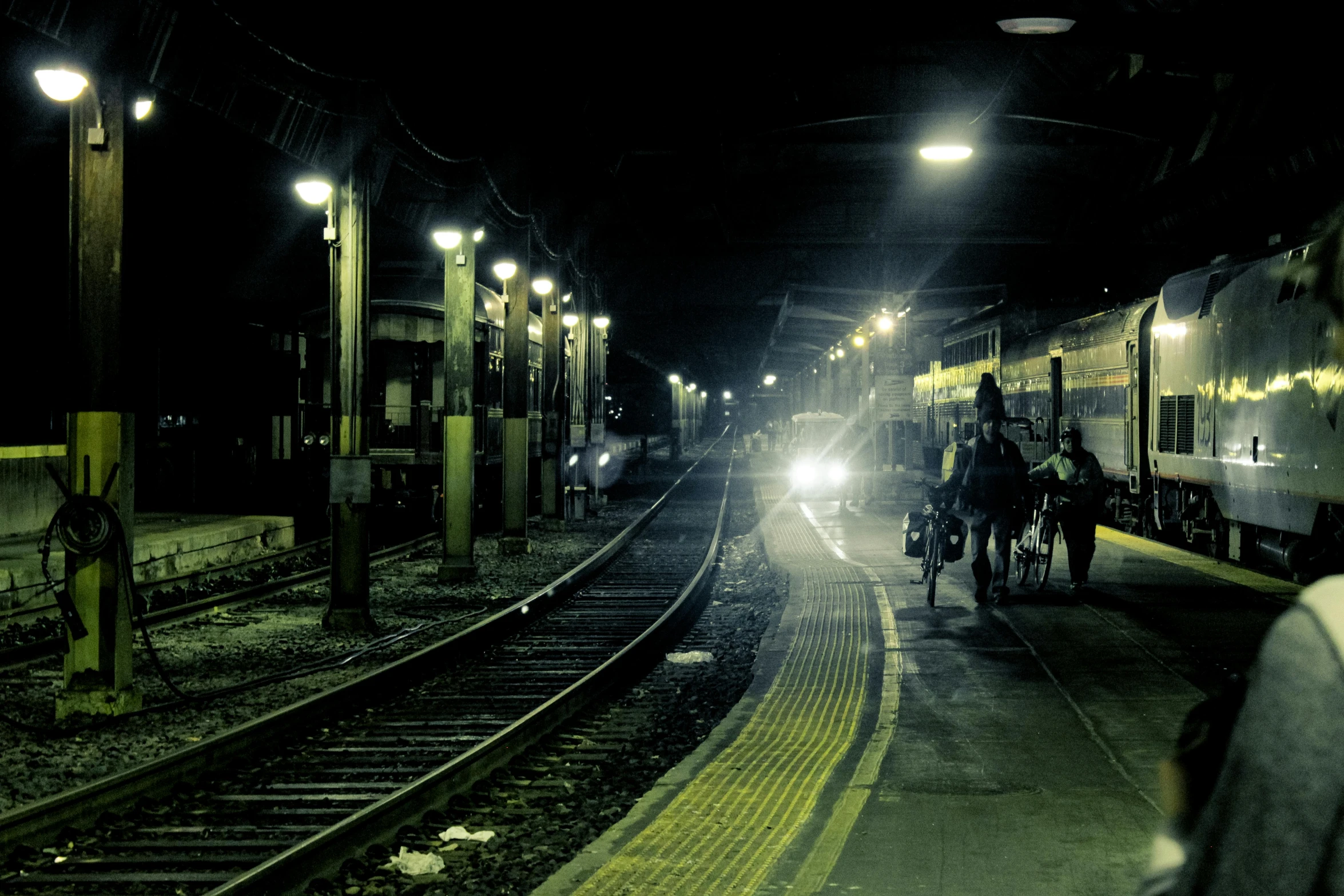 a train pulling into a train station at night, pexels contest winner, lonely rider, people at night, post grunge, desolate :: long shot