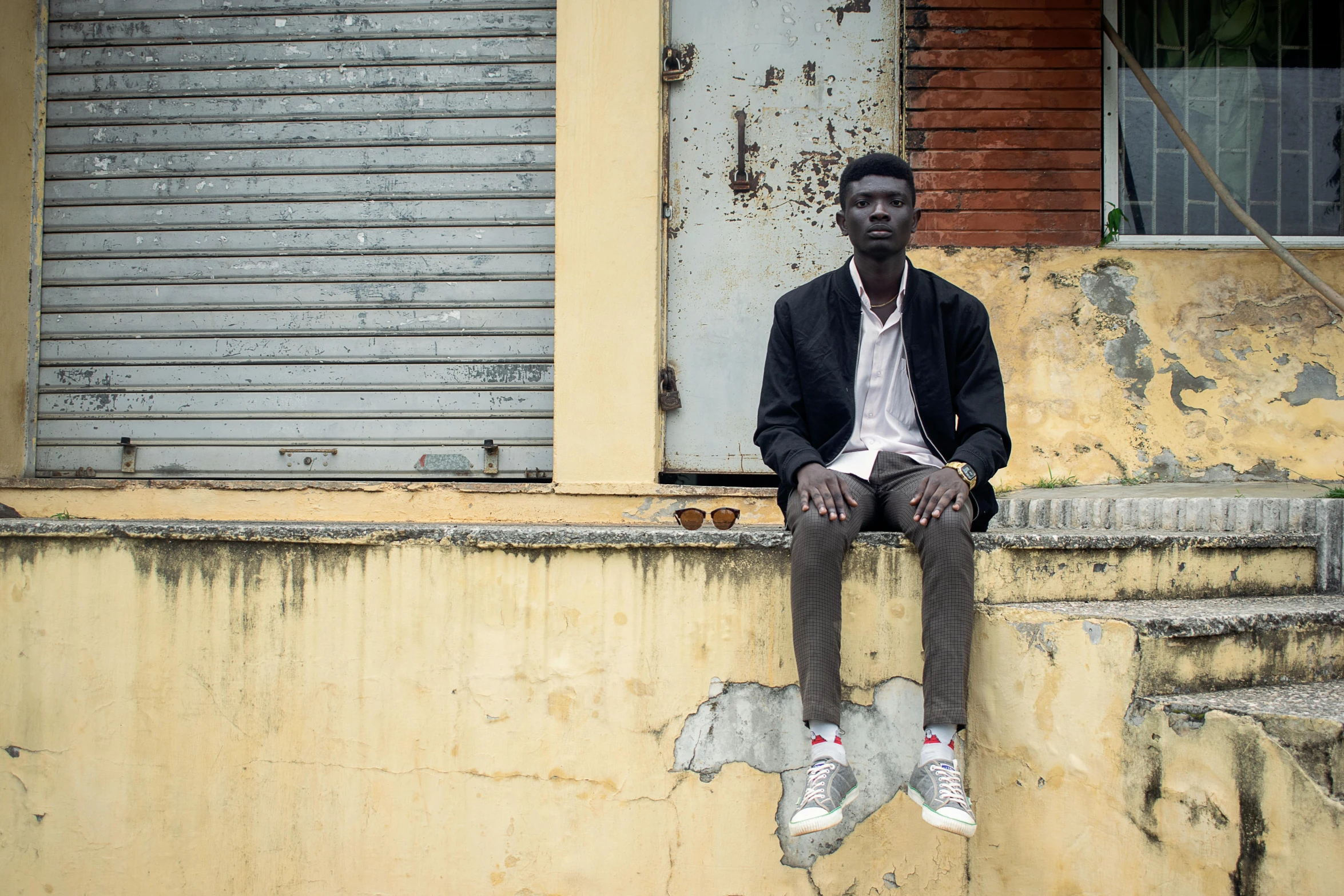 a man sitting on a ledge in front of a building, pexels contest winner, hyperrealism, adut akech, male teenager, 7 feet tall, french man from louisiana