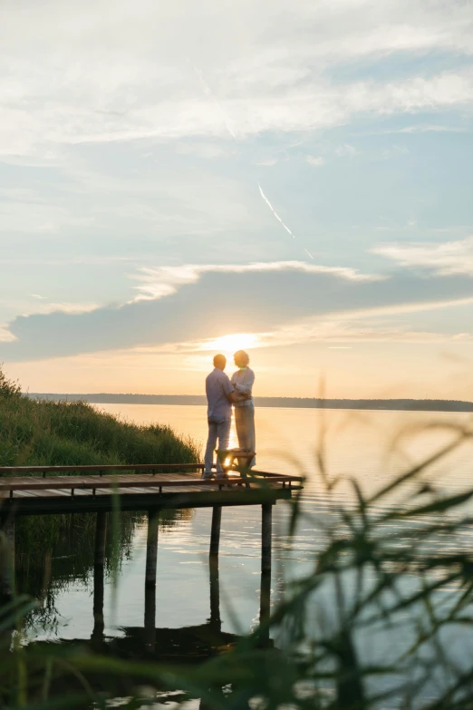 a couple of people that are standing on a dock, by Jan Tengnagel, sunset lighting, midsommar, vista view, happy couple