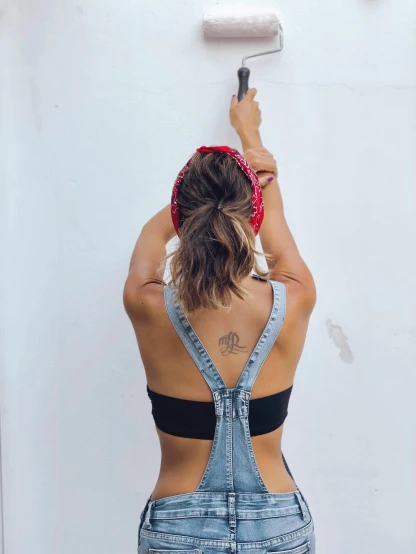 a woman painting a wall with a paint roller, a tattoo, by Olivia Peguero, featured on instagram, wearing a low cut tanktop, back view!!, bandana, outfit photo