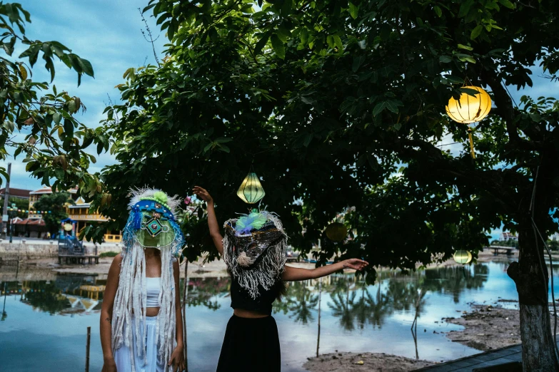 a couple of women standing next to each other, an album cover, unsplash, jellyfish headdress, with paper lanterns, bali, magical garden plant creatures