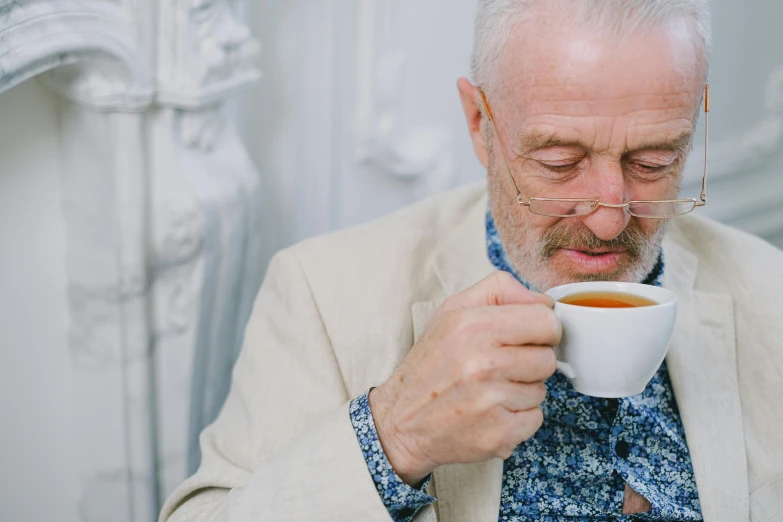 a close up of a person holding a cup of coffee, inspired by John Brown Abercromby, pexels contest winner, hyperrealism, mr robert is drinking fresh tea, short white beard, patterned clothing, frank quitely