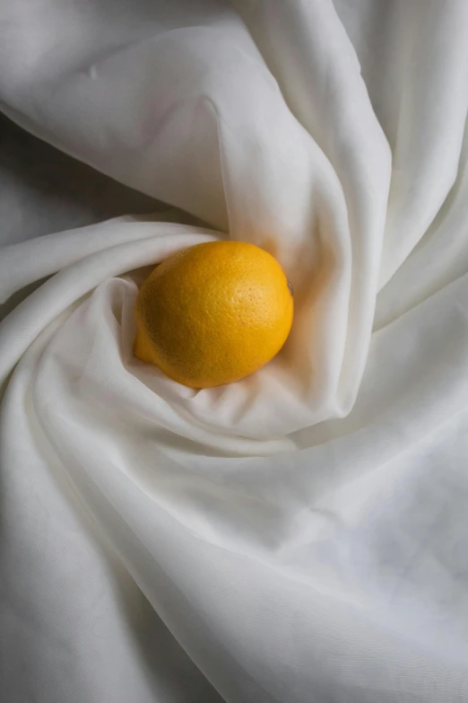 an orange sitting on top of a white cloth, yellow aureole, flowing silk sheets, wearing a lemon, lpoty