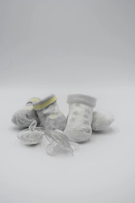 a pair of baby socks laying on top of each other, by Ellen Gallagher, plasticien, incubator medpods, asset on grey background, white and yellow scheme, various items