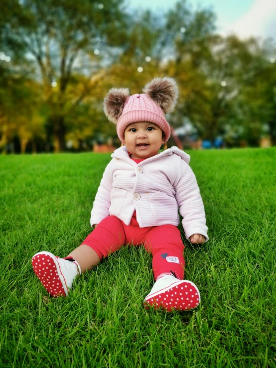 a little girl that is sitting in the grass, a picture, wearing red converse shoes, warm features, pink and red color scheme, at a park
