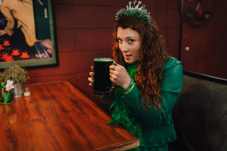 a woman sitting at a table with a glass of beer, ornate dark green clothing, helen the bean queen, irish, 2019 trending photo