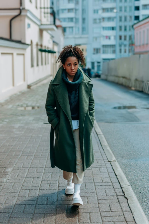 a woman in a green coat walking down a street, pexels contest winner, black young woman, berlin fashion, frontal pose, marine