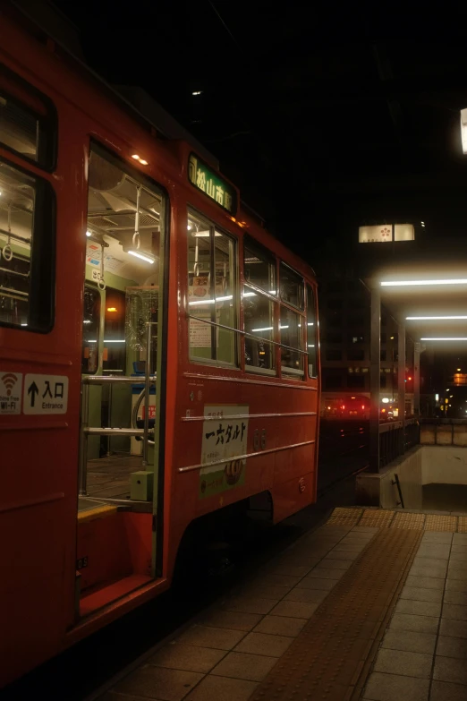 a red train pulling into a train station at night, sōsaku hanga, street tram, high-quality photo, fujifilm”