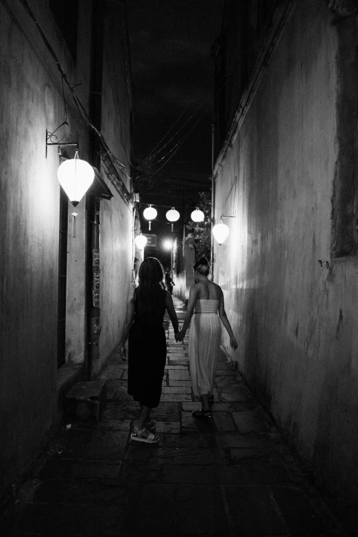 a couple of people that are walking down a street, a black and white photo, inspired by Steve McCurry, unsplash contest winner, happening, evening lanterns, two girls, in style of lam manh, in an alleyway during the purge