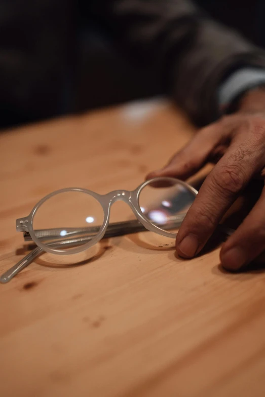a person holding a pair of glasses on a table, slide show, monocle, yukio - e, carefully crafted