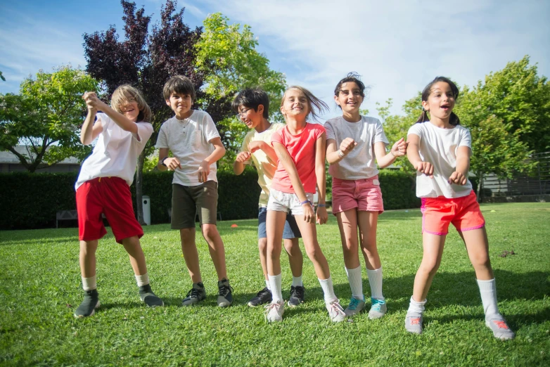 a group of children standing on top of a lush green field, casual playrix games, in spain, wearing shorts and t shirt, dancing a jig