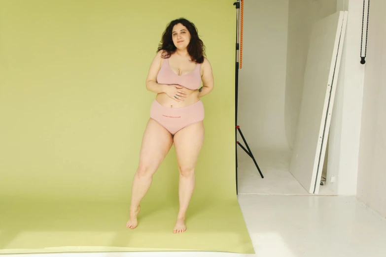 a woman standing in front of a green backdrop, photorealism, pale pink bikini, an obese, on grey background, set photo