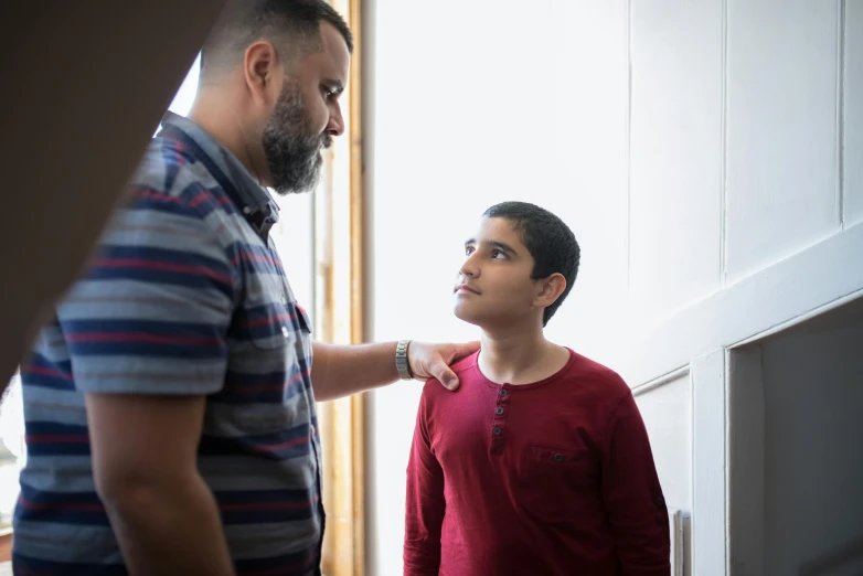 a man standing next to a boy in a room, pexels contest winner, hurufiyya, reassuring, looking partly to the left, te pae, profile image