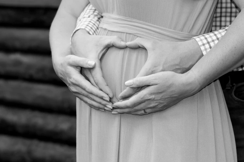 a man and a woman holding hands in the shape of a heart, a black and white photo, by Kristian Zahrtmann, pexels, pregnant belly, closeup photo, advertising photo, maternal