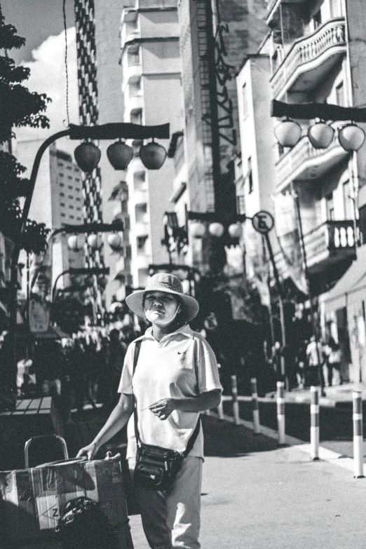 a black and white photo of a man walking down a street, by Naondo Nakamura, she is wearing a hat, in a cybercity, tourist, looking the camera