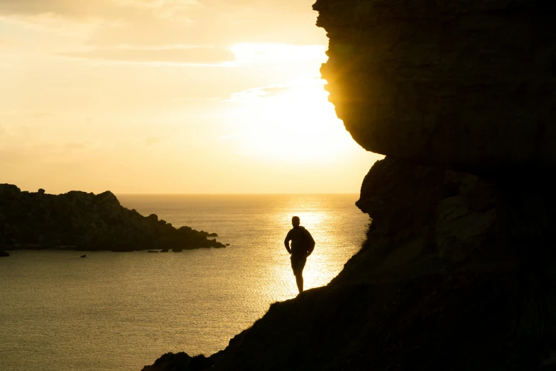 a man standing on top of a cliff next to the ocean, by Simon Marmion, pexels contest winner, romanticism, back lit, cornwall, golden hour 8k, standing in a grotto