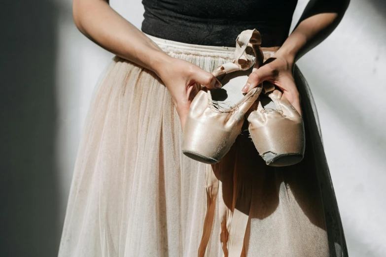 a close up of a person holding a pair of ballet shoes, by Elizabeth Polunin, trending on unsplash, wearing a tutu, made of bronze, clothes torn apart, a person standing in front of a