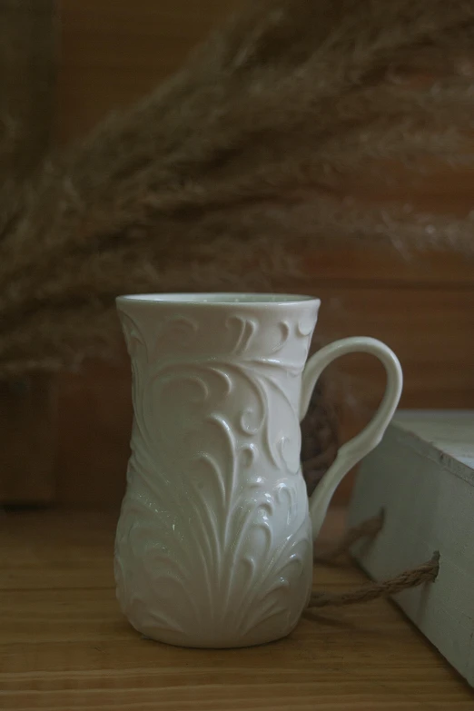 a white vase sitting on top of a wooden table, with a white mug, acanthus scrollwork, shot with sony alpha, embossed