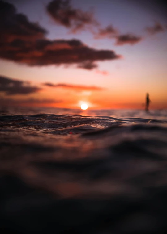 a person standing on a surfboard in the ocean at sunset, by Robbie Trevino, tilt shift”, high quality picture, low angle photo, instagram photo