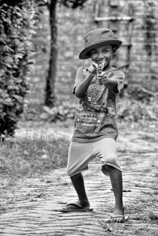 a black and white photo of a young boy, by Joze Ciuha, battle action pose, caracter with brown hat, holding a ray gun, bangladesh