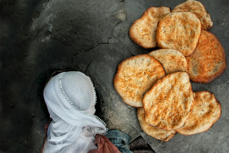 a woman standing next to a pile of bread, inspired by Steve McCurry, pexels contest winner, hurufiyya, flatlay, middle eastern skin, calzone zone, national geographic photo award
