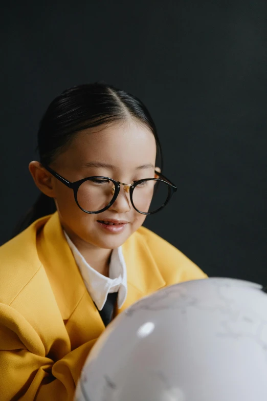 a little girl wearing glasses looking at a globe, inspired by Kanō Naizen, yellow lighting from right, school curriculum expert, monocle, pokimane