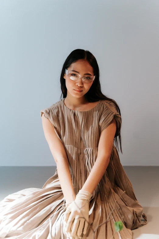 a woman sitting on the floor in a dress, inspired by Kim Tschang Yeul, trending on pexels, gutai group, transparent glasses, light tan, coated pleats, portrait of a young pocahontas