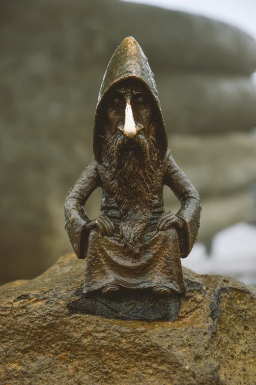 a statue of a man sitting on top of a rock, inspired by Þórarinn B. Þorláksson, unsplash, new sculpture, evil alchemist gnome, symmetrical cloaked figure face, on a candle holder, rusty