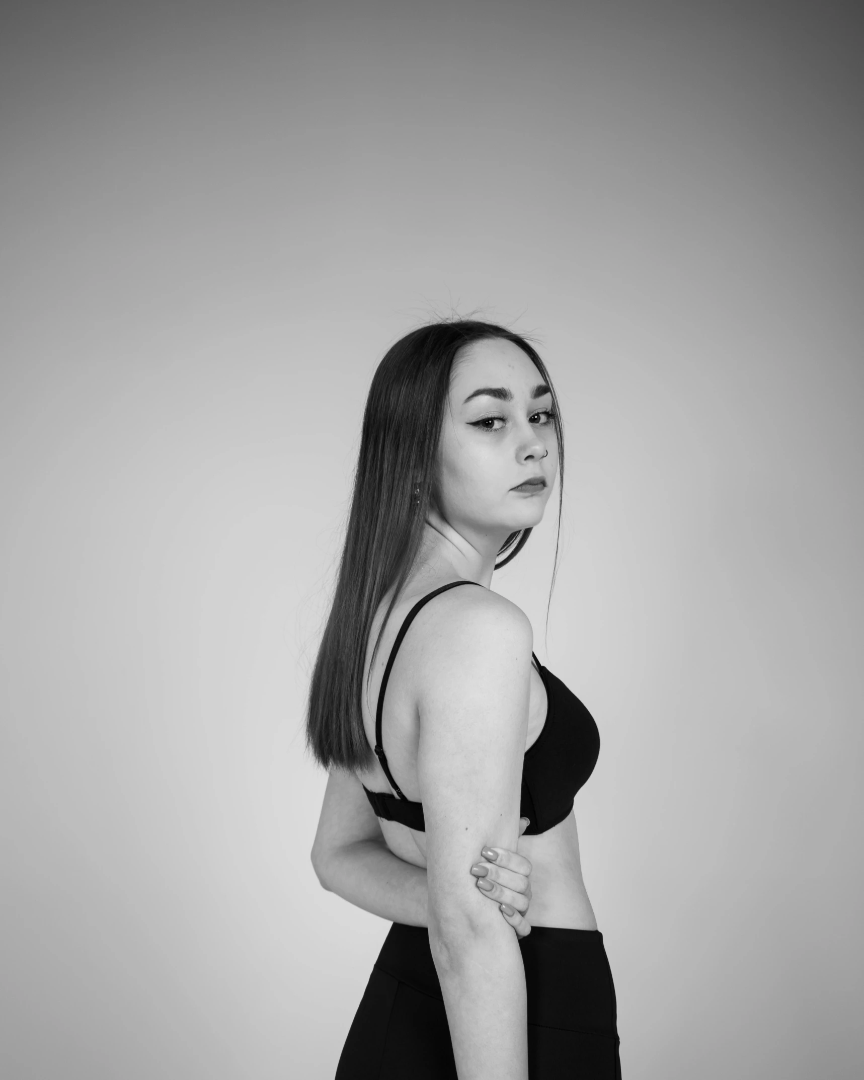 a woman in a black and white photo, a black and white photo, unsplash, wearing a black bodysuit, 18 years old, half body photo, in front of white back drop