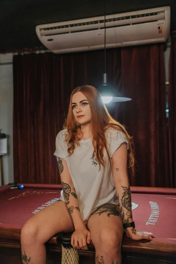 a woman sitting on top of a pool table, a tattoo, inspired by Elsa Bleda, low quality photo, redhead, headshot, trending photo