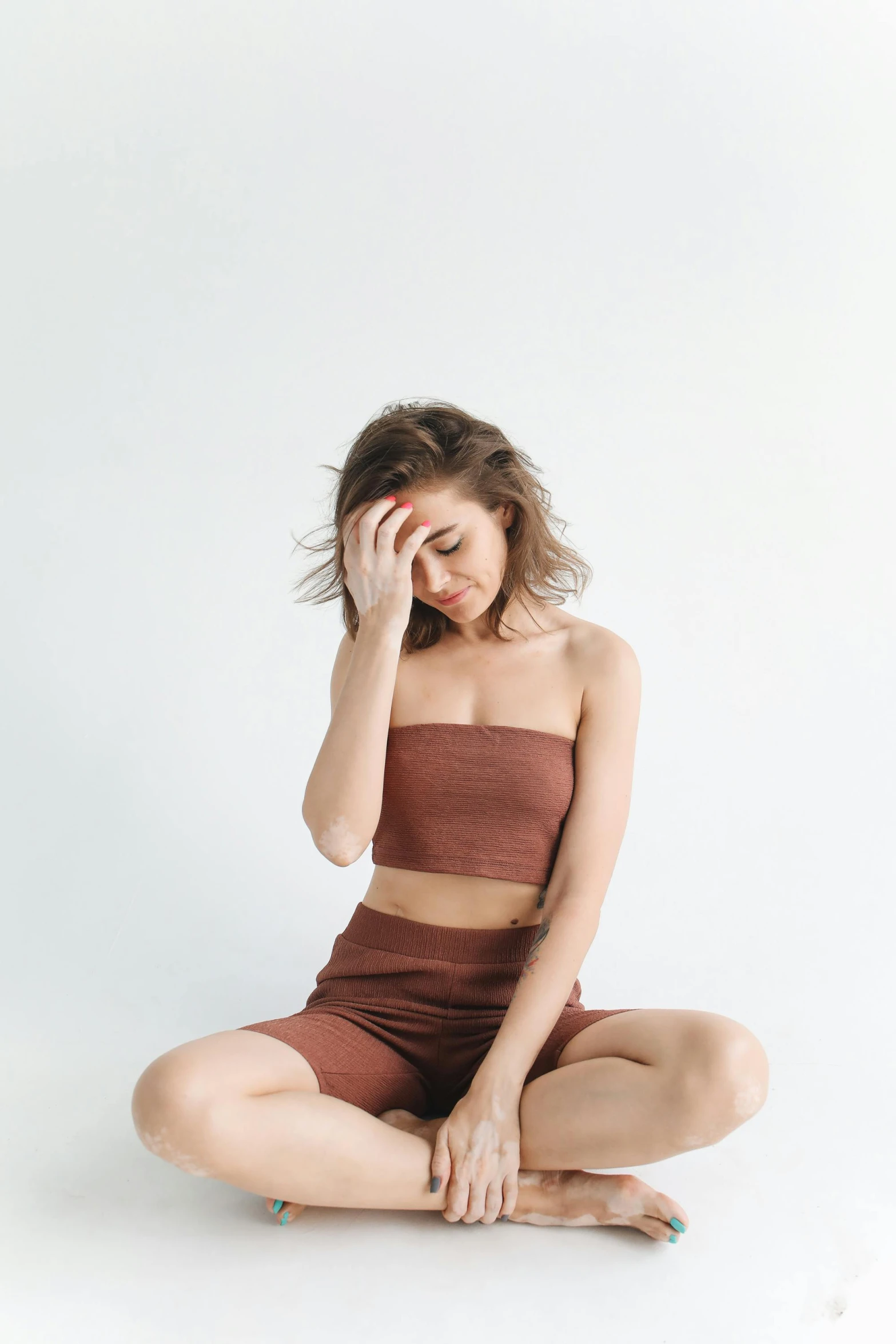 a woman sitting on the floor with her head in her hands, trending on pexels, croptop and shorts, brown:-2, thigh gap, set against a white background