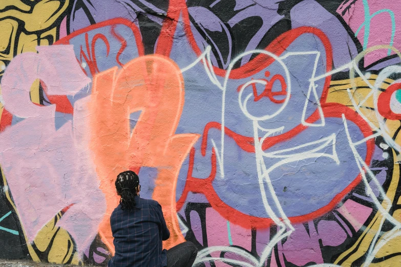 a person sitting in front of a graffiti covered wall, facing away from the camera, colours, filling the frame, illustration »