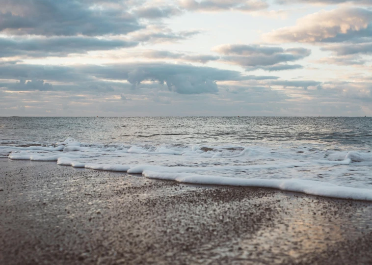 a body of water sitting on top of a sandy beach, by Sophie Pemberton, unsplash, sea foam, early evening, celebrating, on a cloudy day