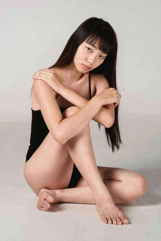 a woman sitting on the ground with her legs crossed, wearing leotard, mei-ling zhou, smooth tan skin, in a photo studio