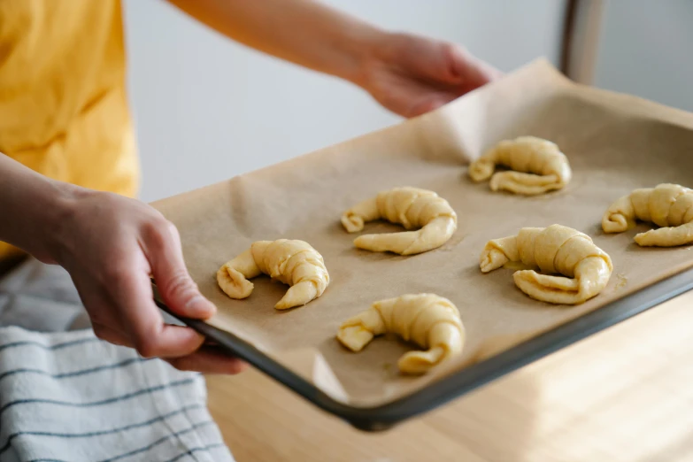 a person holding a tray with croissants on it, inspired by Károly Patkó, trending on pexels, candy worms, for displaying recipes, on parchment, cooking