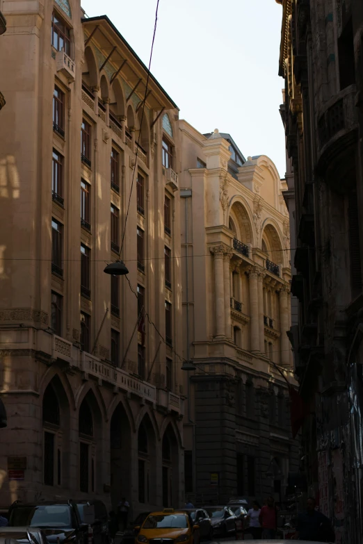 a group of cars driving down a street next to tall buildings, a picture, inspired by Mihály Munkácsy, pexels contest winner, renaissance, lviv historic centre, freddy mamani silvestre facade, street elevation, afternoon sunlight