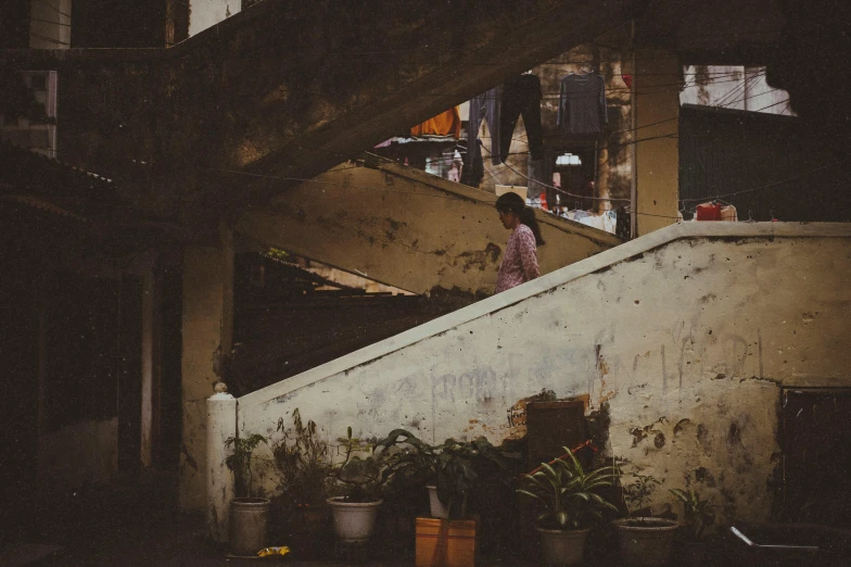 a person walking down a set of stairs, a picture, inspired by Elsa Bleda, pexels contest winner, bengal school of art, slums, vintage photo, brown, flowers around