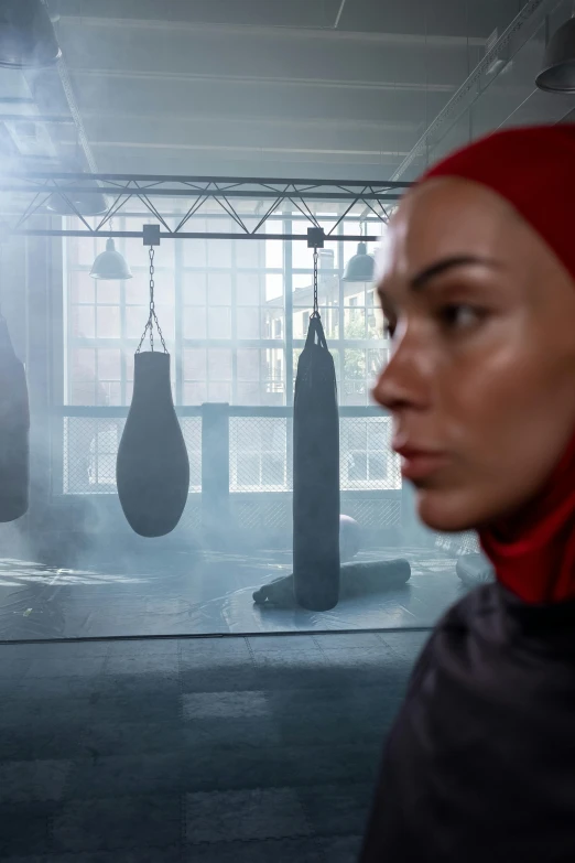 a woman standing in front of a punching bag, inspired by Louisa Matthíasdóttir, hijab, denis villeneuve movie still, in a gym, reflecting