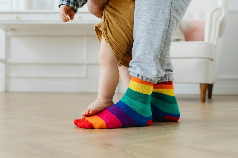 a person standing on top of a wooden floor, inspired by Okuda Gensō, trending on pexels, father with child, striped socks, multi - coloured, toddler