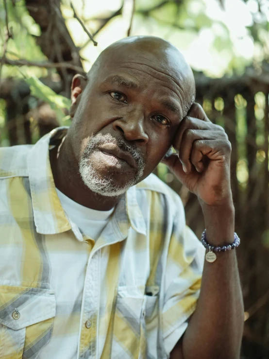 a man in a yellow and white shirt talking on a cell phone, atiba jefferson, amongst foliage, bald head and white beard, looking defiantly at the camera