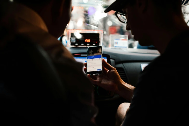 two men sitting in a car looking at a cell phone, by Carey Morris, pexels, happening, square, taxi, avatar image, underexposed
