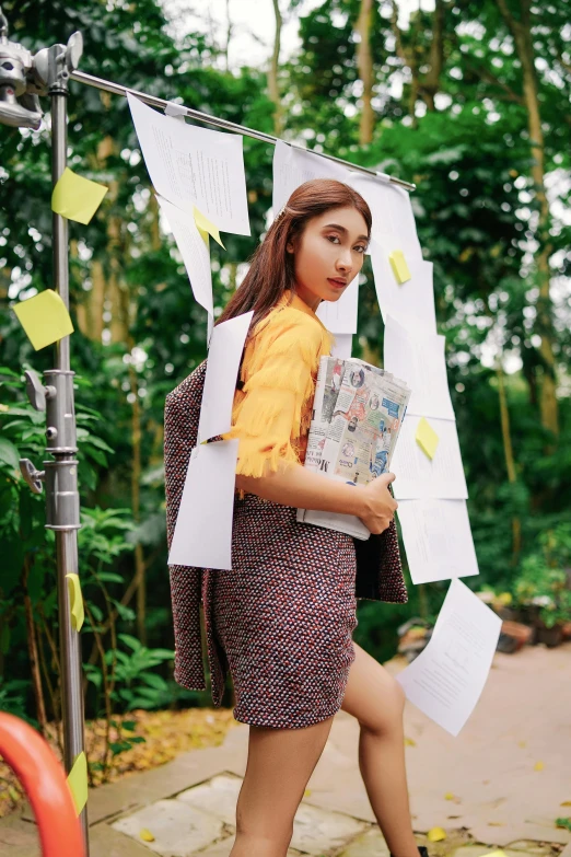 a woman walking down a sidewalk holding a book, a picture, by Ina Wong, trending on pexels, happening, bae suzy, with yellow cloths, toiletpaper magazine, at a fashion shoot